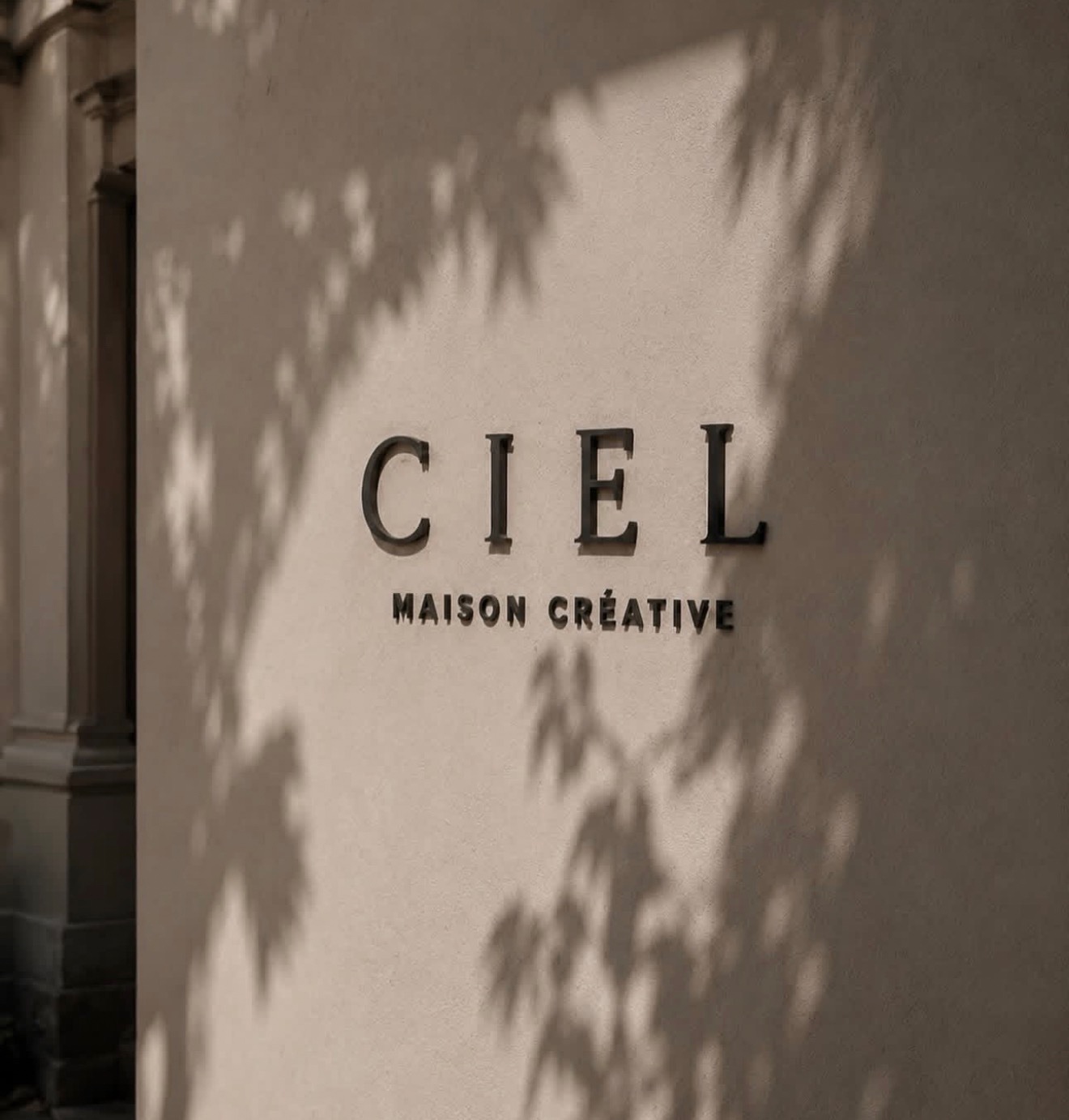 Enseigne « CIEL Maison Créative » sur un mur beige, ombres de feuilles